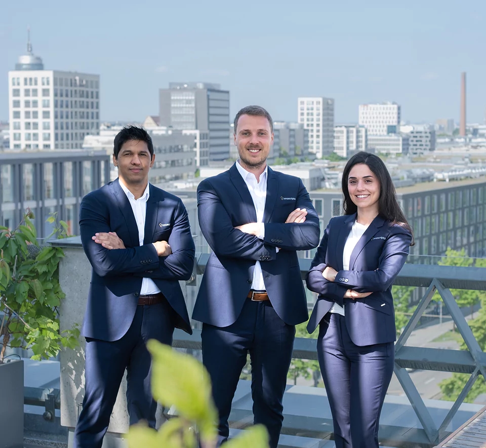 Three business professionals in formal attire standing confidently on a rooftop with a cityscape in the background